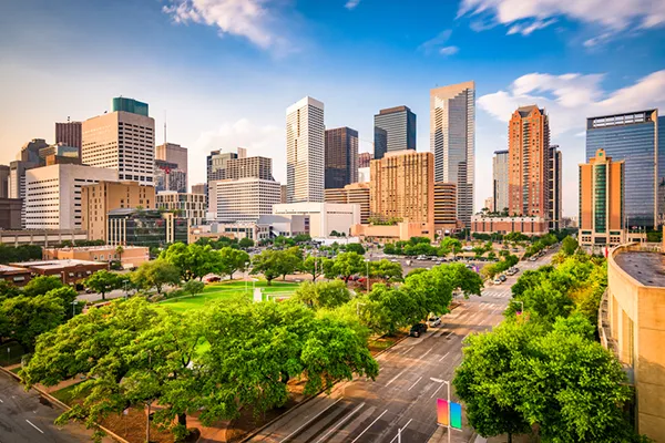Houston skyline with modern skyscrapers, greenery in the foreground, and a clear blue sky, representing the city's vibrant atmosphere and community for legal services like uncontested divorce.