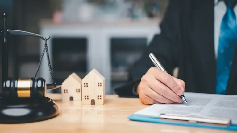 A lawyer sits at a table next to a gavel and a house made of wooden blocks as he reviews a request to modify an uncontested divorce.