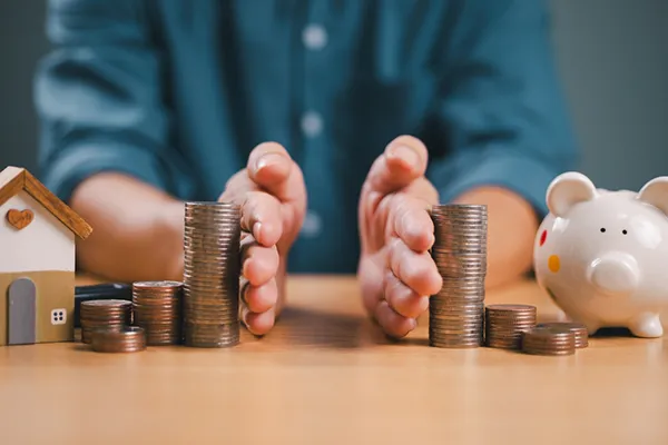 Hands separating stacks of coins, symbolizing property division in an uncontested divorce, with a small house and piggy bank on the table, representing financial assets and savings.