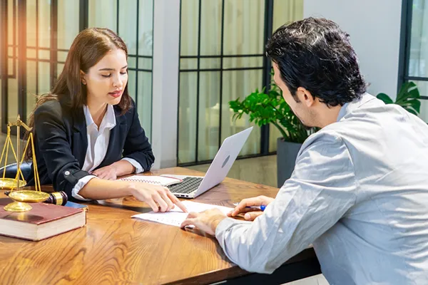 Woman consulting with a client at a desk, discussing divorce paperwork, laptop and legal scales visible, in a law office setting related to uncontested divorce services in Houston.